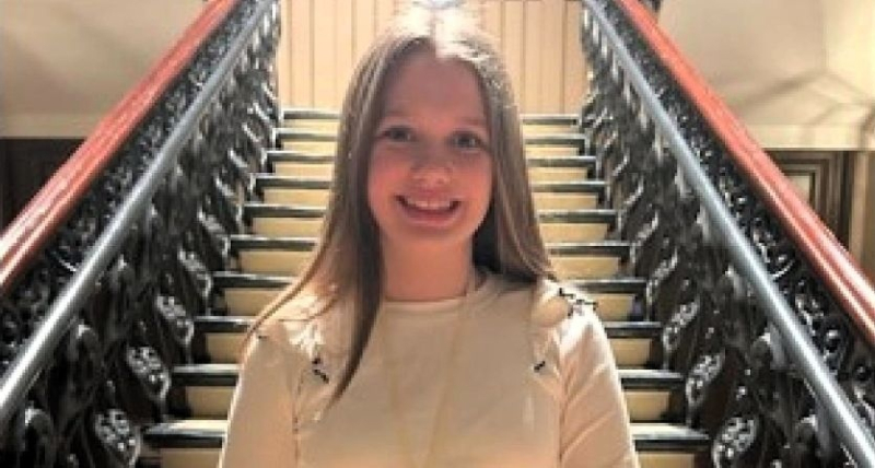 Teenage girl smiling at the foot of a flight of stairs.