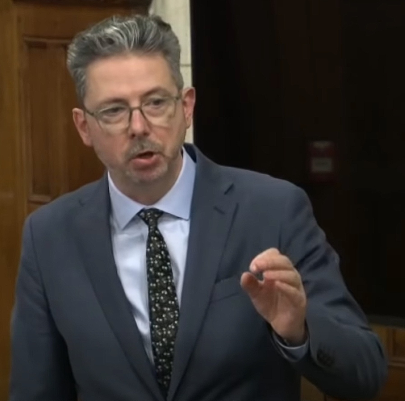 Man in a suit standing up speaking during a debate.
